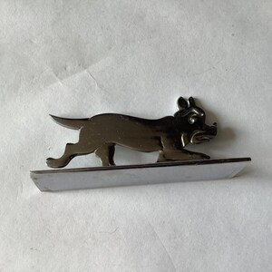 Pode incluir: Uma figura de c&atilde;o cromada, retratada em pose de corrida, montada numa base retangular. As caracter&iacute;sticas do c&atilde;o s&atilde;o detalhadas, com orelhas, focinho e patas vis&iacute;veis. A pe&ccedil;a tem uma superf&iacute;cie reflexiva.