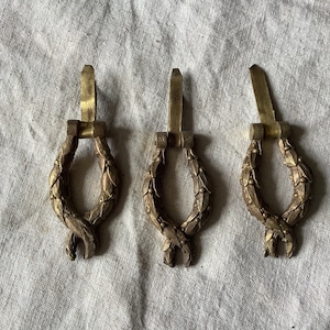 May include: Three antique brass door or cabinet pulls with a decorative wreath design.