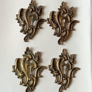 Puede incluir: Cuatro cubiertas de cerradura antiguas de latón con diseños ornamentados y arremolinados. Cada cubierta presenta un ojo de cerradura en el centro y adornos decorativos. El latón tiene una pátina cálida y envejecida.