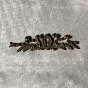 Puede incluir: Una tapa de mirilla decorativa de metal con un diseño floral. La tapa está hecha de latón y tiene una mirilla en el centro.