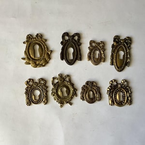 Peut inclure: Collection de huit cache-trous de serrure anciens en laiton. Les cache-trous de serrure présentent des motifs ornés, notamment des nœuds, des couronnes de laurier et des cadres décoratifs. Les cache-trous de serrure sont dans diverses nuances d'or et de bronze.