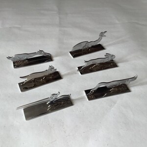 Pode incluir: Uma cole&ccedil;&atilde;o de seis figuras de animais em metal prateado, incluindo um c&atilde;o, um coelho e um p&aacute;ssaro, cada uma montada numa base retangular. As figuras est&atilde;o numa pose de corrida ou salto, com detalhes.