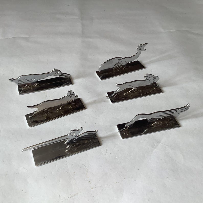 Pode incluir: Uma cole&ccedil;&atilde;o de seis figuras de animais em metal prateado, incluindo um c&atilde;o, um coelho e um p&aacute;ssaro, cada uma montada numa base retangular. As figuras est&atilde;o numa pose de corrida ou salto, com detalhes.