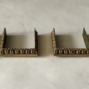 May include: Five gold-colored metal corner brackets with an ornate design. The brackets are all the same size and shape.