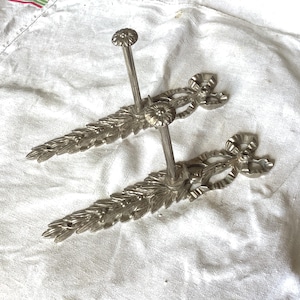 Può includere: Due portasciugamani da parete in metallo argentato con decorazioni floreali ornate. Ogni portasciugamani ha un'unica asta.