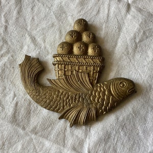 May include: A gold-colored metal fish with a basket of round objects on its back. The fish has a detailed design and is a decorative piece.