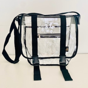 Puede incluir: Bolso mensajero transparente de pl&aacute;stico con correas y hebillas negras. El bolso tiene un bolsillo con cremallera en la parte delantera.