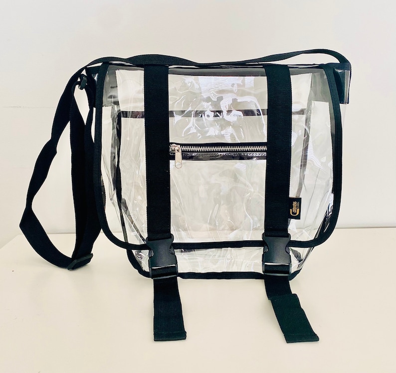 Puede incluir: Bolso mensajero transparente de pl&aacute;stico con correas y hebillas negras. El bolso tiene un bolsillo con cremallera en la parte delantera.