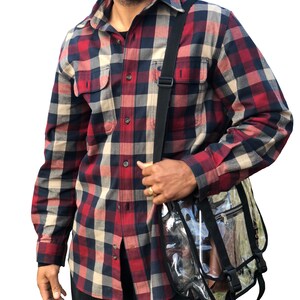 Puede incluir: Un hombre con una camisa de franela a cuadros rojos, negros y blancos con una bolsa de mensajero de pl&aacute;stico transparente con correas negras.