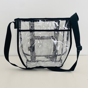Puede incluir: Una bolsa de mano transparente de pl&aacute;stico con una correa de hombro negra ajustable. La bolsa tiene un ribete negro y un bolsillo con cremallera en la parte delantera.