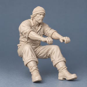Puede incluir: Una figura a escala de color beige monocrom&aacute;tico que representa a una persona barbuda con gorro de punto, camisa de cuello con mangas remangadas, tirantes, pantalones y botas pesadas, en posici&oacute;n sentada con los brazos extendidos.