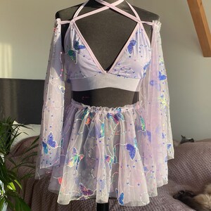 May include: A lavender-colored mesh top and skirt set with butterfly embroidery. The top has a halter neckline and long sleeves. The skirt is a mini skirt with a ruffled hem.