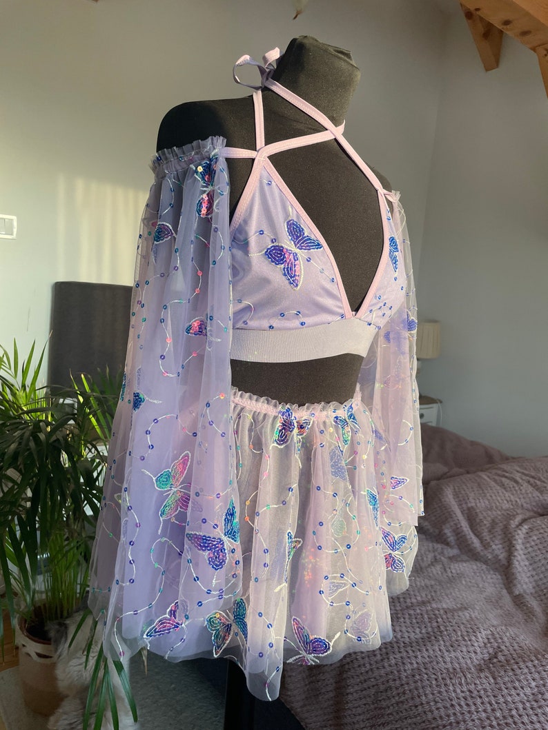 May include: A lavender-colored two-piece outfit with butterfly embellishments. The top is a halter style with a mesh fabric and the skirt is a tulle skirt with a ruffled hem.