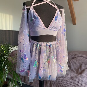 May include: A lavender-colored mesh top and skirt set with butterfly embellishments. The top is a halter style with a criss-cross strap design. The skirt is a mini skirt with a ruffled hem.