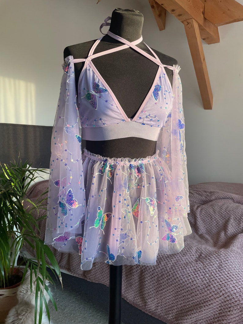May include: A lavender-colored mesh top and skirt set with butterfly embellishments. The top is a halter style with a criss-cross strap design. The skirt is a mini skirt with a ruffled hem.