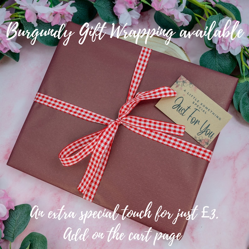May include: A square gift box wrapped in solid burgundy paper, tied with a red and white gingham ribbon bow. A small rectangular kraft paper tag is attached, featuring the printed text A LITTLE SOMETHING SPECIAL Just For You with floral accents.
