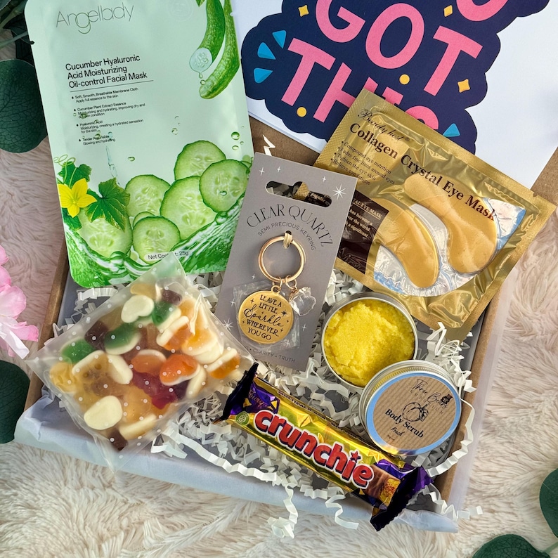May include: A gift box filled with self-care items. Includes a cucumber face mask, collagen eye masks, a gold keychain with the text "Leave a little sparkle wherever you go", a Crunchie candy bar, and a body scrub.