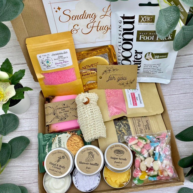 May include: A gift box containing a variety of self-care items including a pink bath soak, coconut foot mask, soap bar, exfoliating pouch, hand and body cream, shower souffle, sugar scrub, herbal tea, and a bag of colourful gummy sweets.