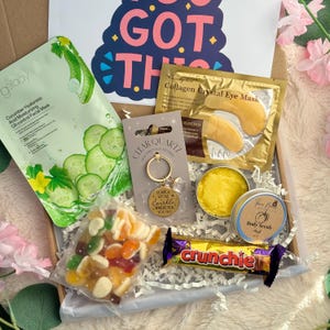 May include: A gift box filled with self-care items. Includes a cucumber facial mask, eye masks, a keychain with the text "Leave a little sparkle wherever you go", body scrub, candy, and a Crunchie candy bar.