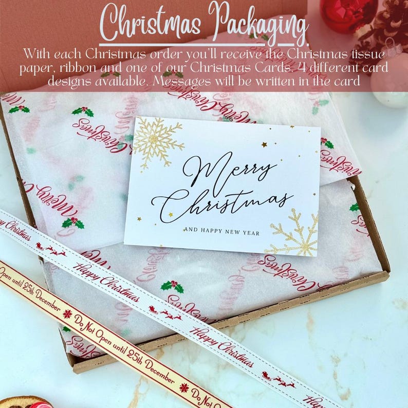 May include: A cardboard box containing white tissue paper with red and green holly and Merry Christmas text, a white greeting card with gold snowflakes and Merry Christmas and Happy New Year text, and a ribbon with Happy Christmas text.