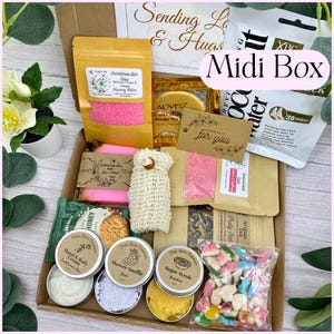 May include: A cardboard gift box containing various items including a yellow pouch of bath salts, a pink soap bar, a beige mesh bag, a coconut water foot mask, a bag of fruit-shaped sweets, and small round tins of hand cream, shower souffl&eacute;, and sugar scrub.