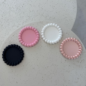 May include: Four round phone grips with a beaded edge. The grips are in black, white, pink, and light pink.