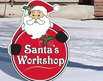 Könnte beinhalten: Ein rot-weißes Schild mit Santa Claus und dem Text "Santa's Workshop". Das Schild hat einen roten Kreis mit weißem Text und einem schwarzen Rand. Santa trägt einen roten Hut und Anzug mit weißem Bart und schwarzen Handschuhen. Das Schild ist auf einem Metallpfahl.