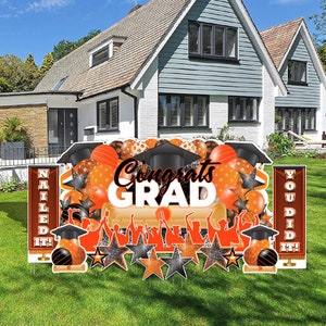 May include: Orange and black graduation yard sign set with the words "Congrats Grad", "You Did It!" and "Nailed It!"  The set includes a variety of decorations, including stars, balloons, and graduation caps.