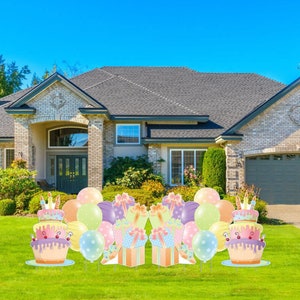 May include: A birthday party yard sign set with two large cake cutouts, two gift boxes, and balloons. The cakes are decorated with pink, yellow, and blue frosting and candles. The gift boxes are wrapped in colorful paper with bows. The balloons are pink, yellow, and blue.
