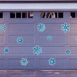 May include: A gray garage door decorated with blue snowflake decals. The door has a window in each section. The house number 1156 is visible on the right side of the door.
