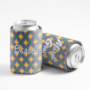 May include: Two can coolers with a Mardi Gras theme. The coolers are decorated with a purple, green, and gold diamond pattern. One cooler has the text "Beads?" and the other has the text "Mardi Gras".