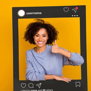 May include: A woman with curly hair smiles and gives a thumbs up while posing in front of a black Instagram frame. The frame has a username, a heart, a paper airplane icon, and the text "liked by name and 00 others".