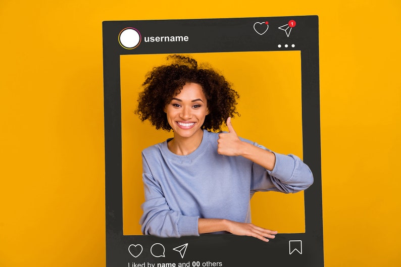 May include: A woman with curly hair smiles and gives a thumbs up while posing in front of a black Instagram frame. The frame has a username, a heart, a paper airplane icon, and the text "liked by name and 00 others".