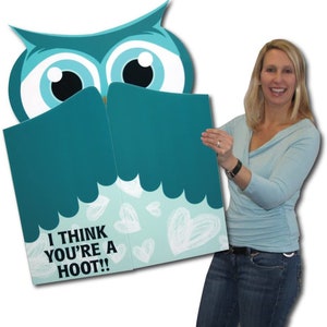 May include: A teal owl-shaped greeting card with the text "I THINK YOU'RE A HOOT!!" and white heart doodles. The card is held open, revealing the inside. The owl has large eyes and a friendly expression.