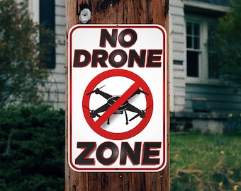May include: A rectangular "NO DRONE ZONE" sign with a red circle and a drone symbol crossed out. The sign is mounted on a weathered wooden pole. The text is in black with a white background and a red border.