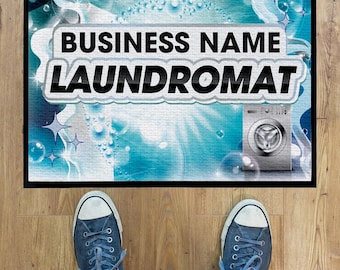 May include: A black welcome mat with a blue and white swirling design. The text "BUSINESS NAME LAUNDROMAT" is printed in white on the mat. A silver washing machine is visible in the background.