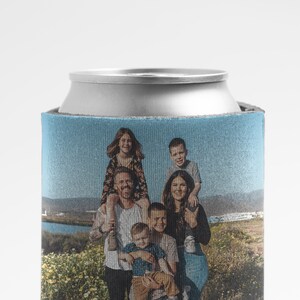 K&ouml;nnte beinhalten: Ein blauer und wei&szlig;er Getr&auml;nkedosenk&uuml;hler mit einem Foto einer sechsk&ouml;pfigen Familie, die in einem Blumenfeld steht. Die Familie l&auml;chelt und schaut in die Kamera.