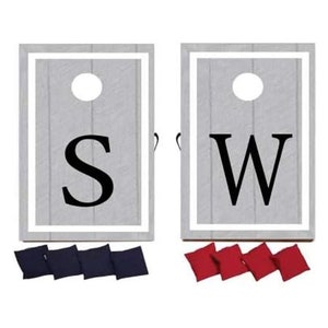 May include: A cornhole game set featuring two gray wooden boards with white borders. Each board has a large black letter, "S" and "W", and a white hole. Includes four navy blue and four red bean bags.