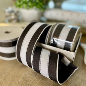 May include: Decorative ribbon rolls featuring a striking black and white striped design. The image shows the ribbon in a box and on a roll, highlighting its texture. Ideal for crafting and gift wrapping projects.