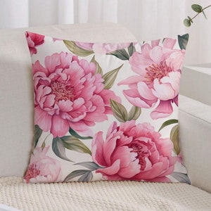 May include: A white cushion with a pink floral pattern. The cushion features large pink peonies with green leaves on a white background.