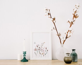 May include: A white framed print of a watercolor painting of pink and green flowers, a white candle in a teal candle holder, and a white vase with a branch of cotton flowers. The items are arranged on a light brown wooden surface.