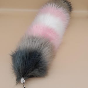 May include: A fluffy, multi-colored tail accessory. The tail transitions from dark gray to light gray, pink, white, and back to gray. It has a silver-colored clasp attached to a white cord.