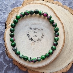 May include: A green and pink gemstone bracelet with a handmade tag that says "Handmade by Jay".