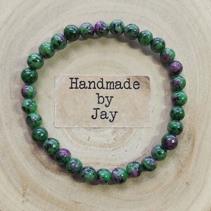 May include: A green and pink gemstone bracelet with a handmade tag that reads "Handmade by Jay".