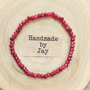 May include: A red gemstone bracelet with faceted beads. The bracelet is handmade and has a tag that says "Handmade by Jay".