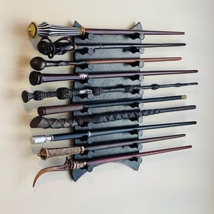 May include: A black wall-mounted wand holder with 10 wands of various colours and styles. The holder has a decorative design and is made of wood.