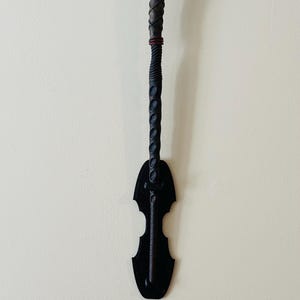May include: A black metal wall mount with a decorative design, holding a black and brown twisted wooden staff.