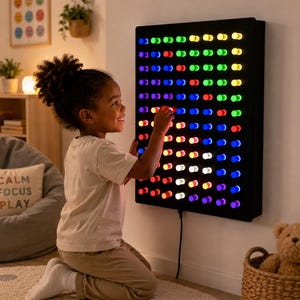 Peut inclure: Un panneau lumineux rectangulaire noir fixé au mur, doté d'une grille de nombreux taquets cylindriques qui s'illuminent de différentes couleurs, notamment rouge, bleu, vert, jaune et blanc. L'appareil est alimenté par un cordon noir.