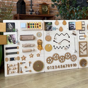 Op de afbeelding: Een houten sensorisch bord met diverse interactieve elementen voor kinderen. Het bevat tandwielen, doolhoven, vormen en cijfers. Het bord is ontworpen om de fijne motoriek en sensorische exploratie te stimuleren. Het bord is gemaakt van lichtgekleurd hout.