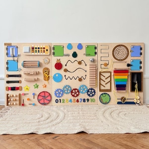 May include: A wooden activity board with various interactive elements for children. Features include latches, gears, a maze, a rainbow-colored block set, and a bead maze. The board is designed to promote fine motor skills and sensory exploration.